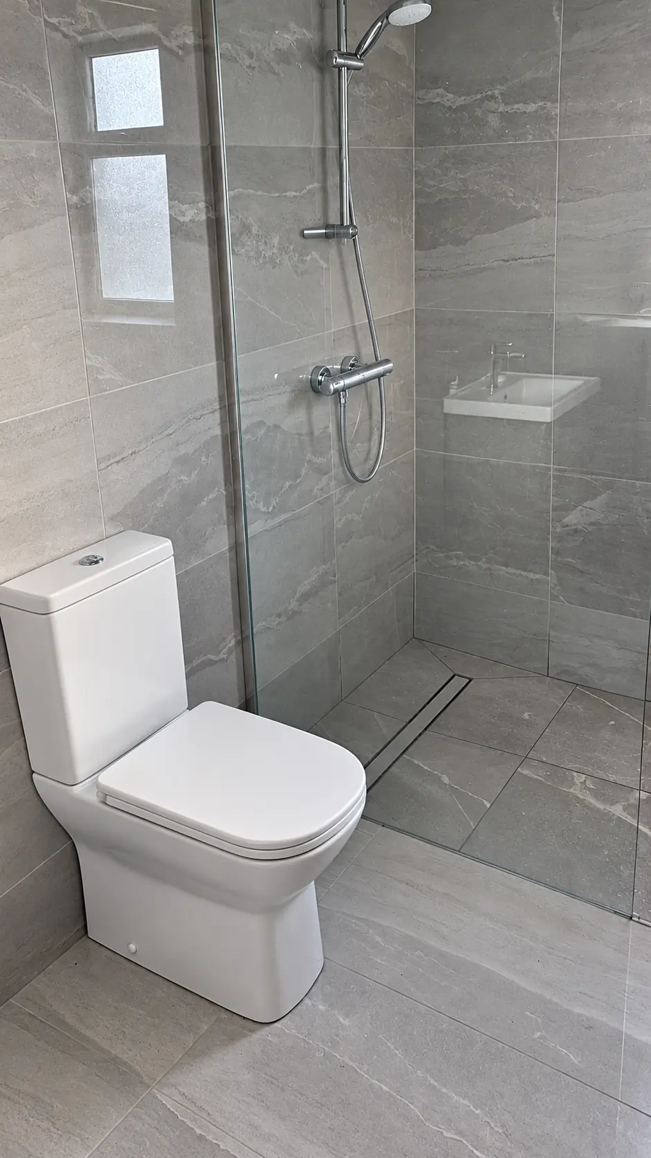 Grey tiled bathroom with glass walk-in shower and white toilet