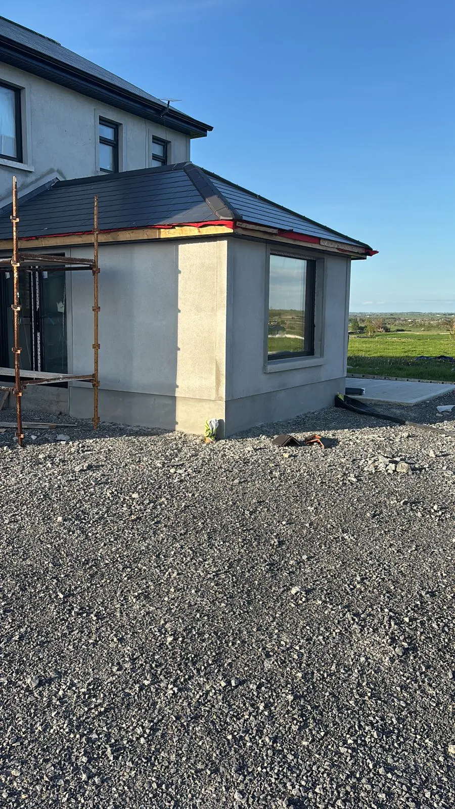 Rendered house extension with hipped roof, scaffolding and unfinished fascia
