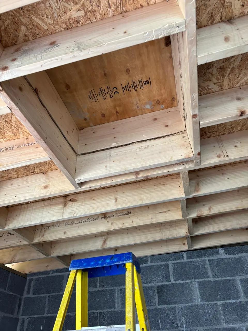 Timber joists and framing opening above a yellow ladder
