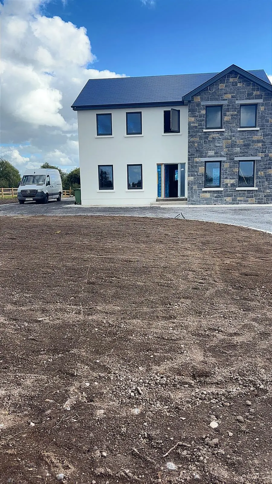Two-storey stone and white render house with unfinished entrance and groundworks