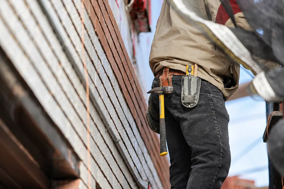 Construction worker carrying tools beside a brick wall